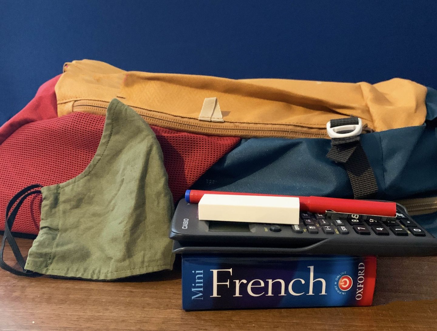 Back to school. School bag with face mask, book, calculator and pen.