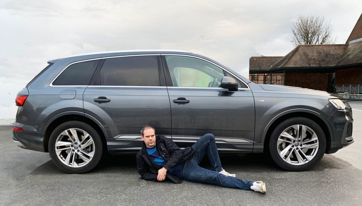 John Adams of Dadbloguk lying down next to an Audi hybrid Q7.