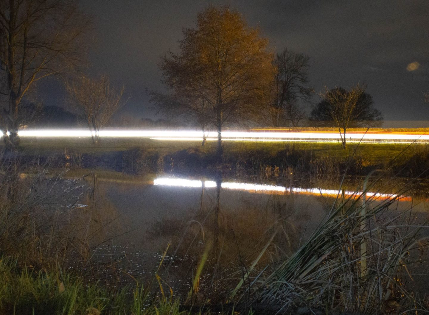 Experimental long-exposure image of car reflected in a pond.