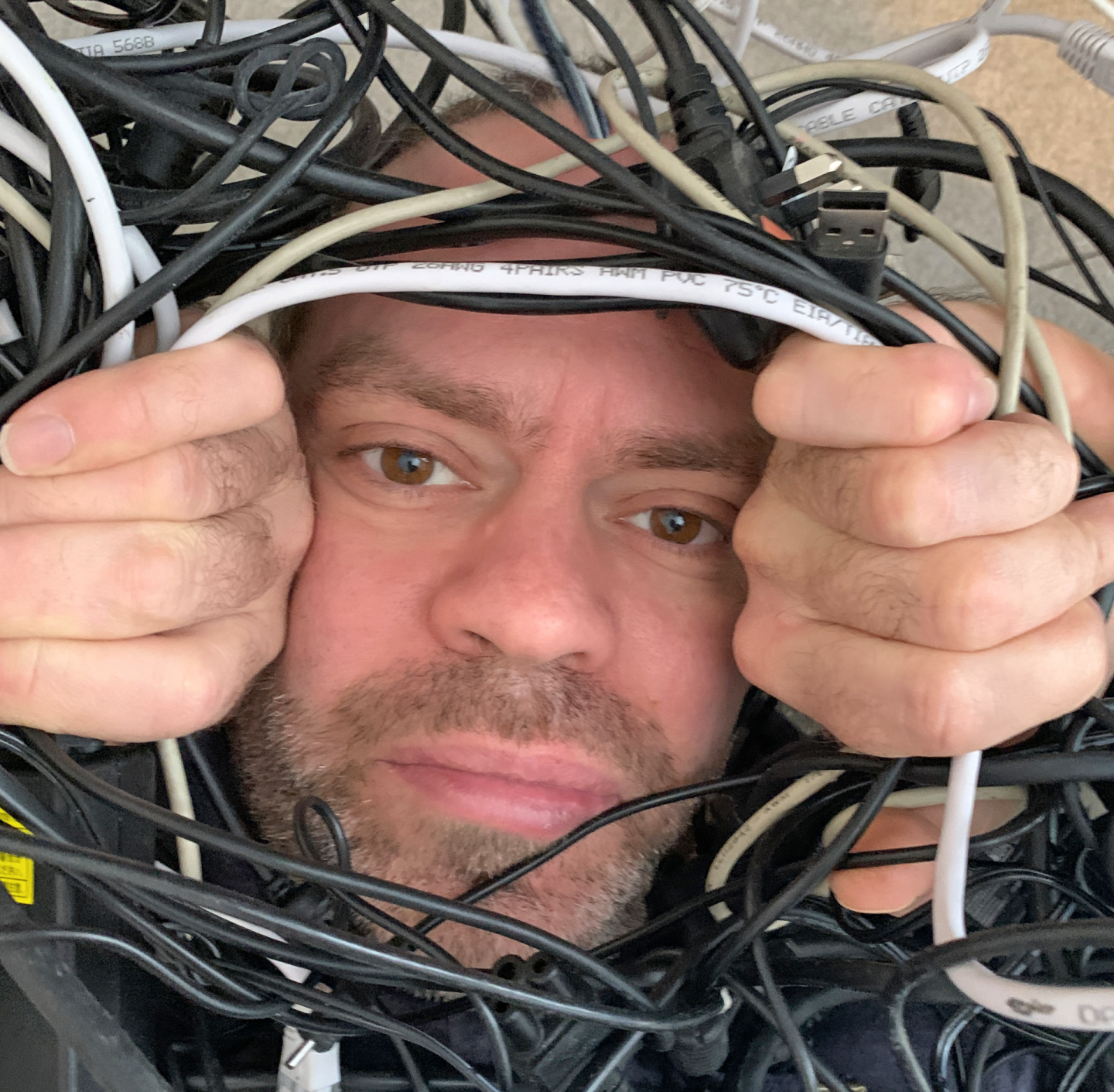 Man surrounded by wires while helping his children with home learning.