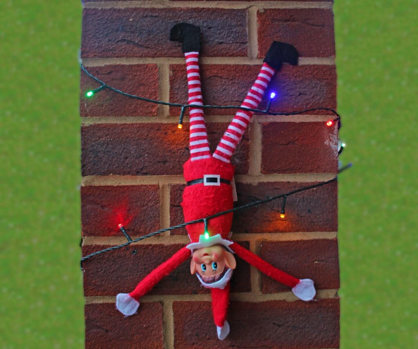 Elf on the Shelf tied to a wall with Christmas lights. 
